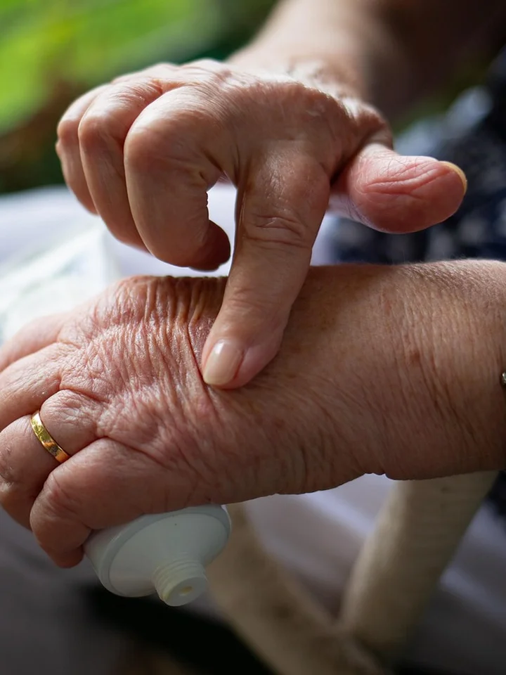Close-up of hands applying moisturizer from a small white bottle onto the skin.