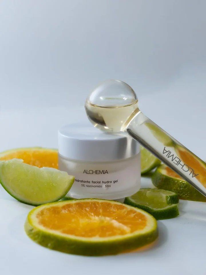 A skincare jar with a dropper bottle and sliced citrus fruits (orange and lime) on a clean white surface.