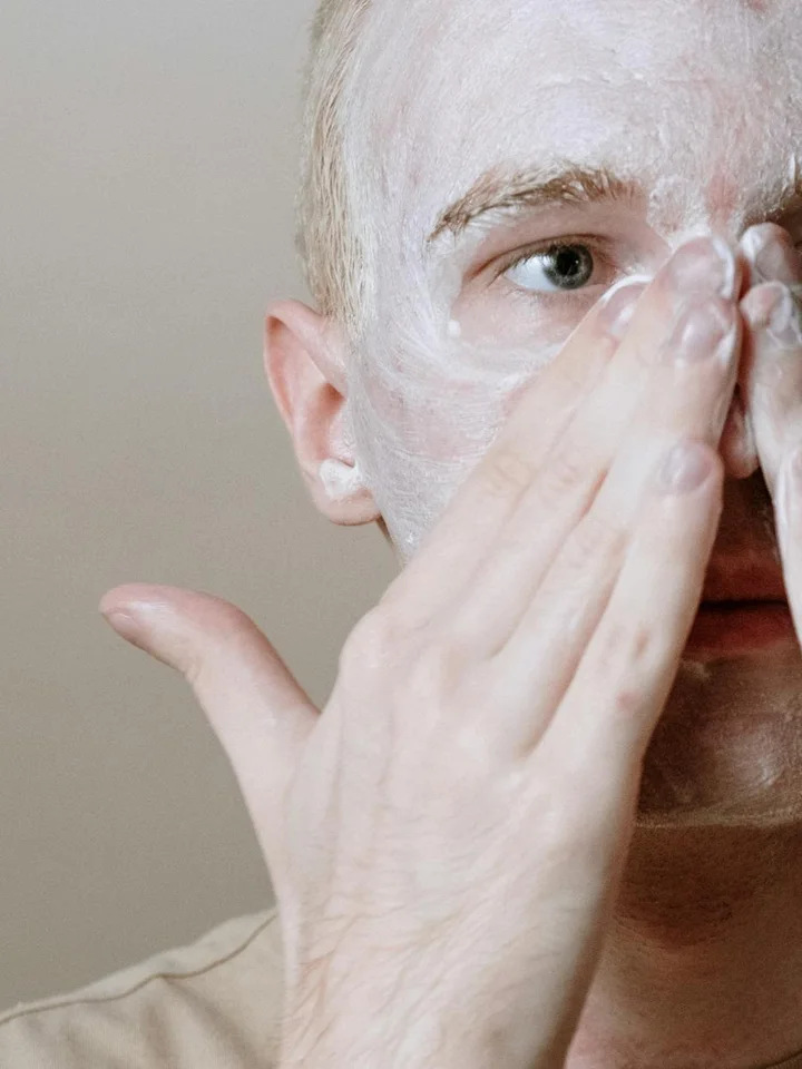 Close-up of a person applying a white facial mask on their face.