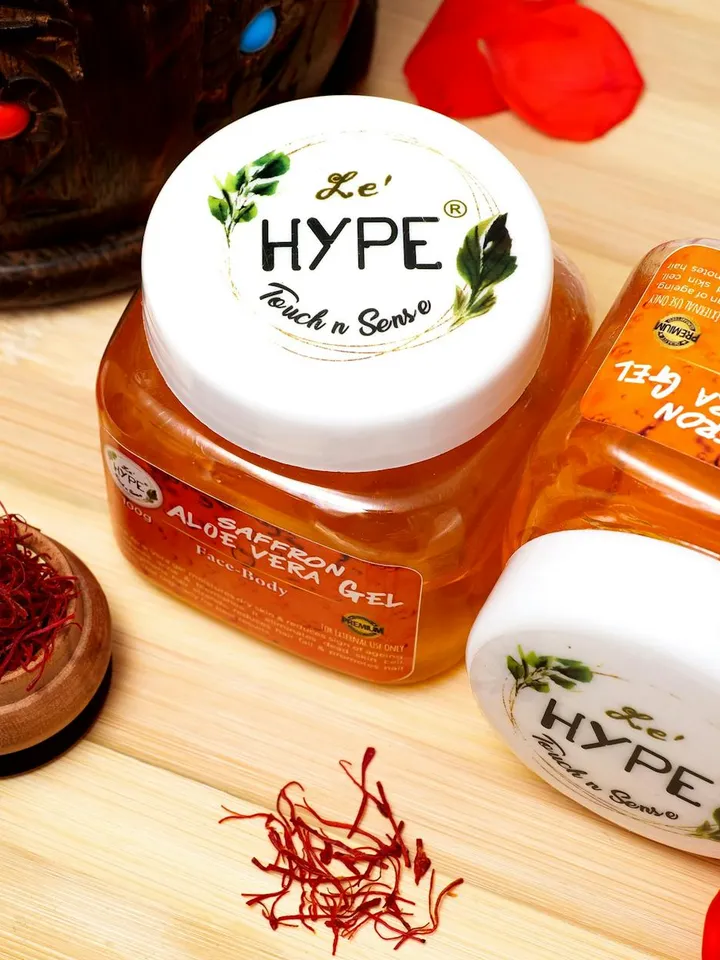 Two jars of aloe vera gel on a wooden surface with red petals nearby.