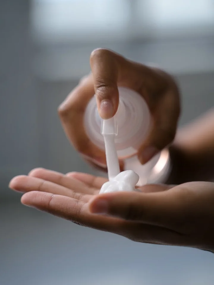 Close-up of hands applying a white cream from a pump onto the palm, representing topical acne treatment