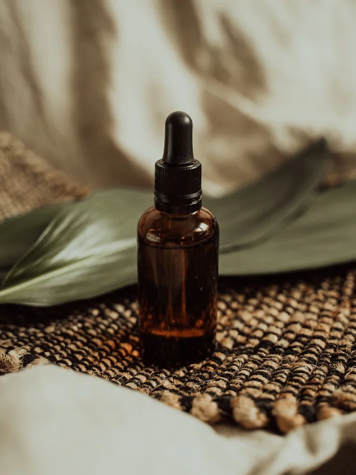 Amber glass dropper bottle on a woven natural backdrop with a green leaf in the background, representing skincare serum packaging.