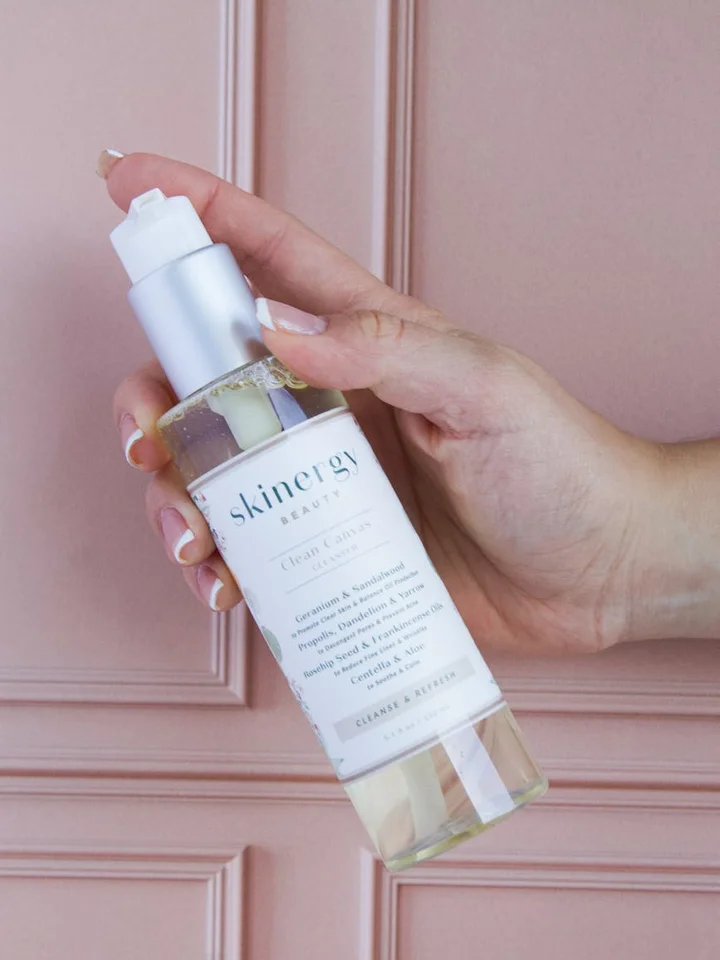 A hand holding a clear pump bottle of skincare serum against a pale pink background, illustrating application guidance for alpha arbutin.