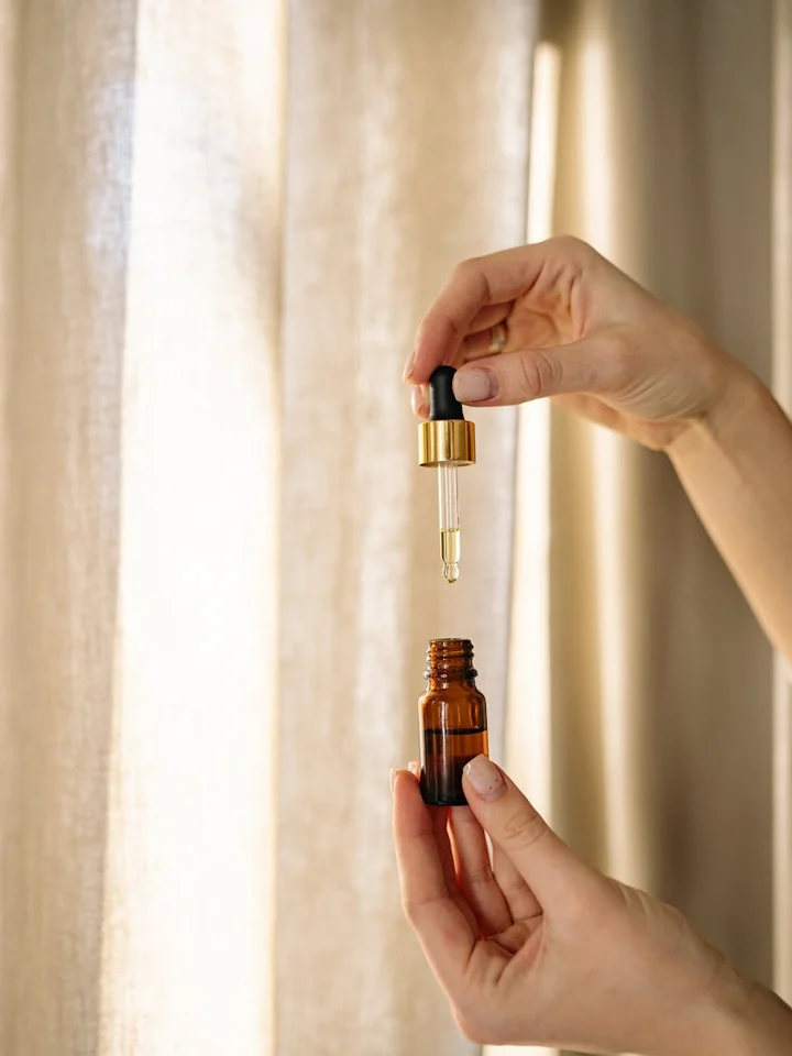 A person's hands dispensing azelaic acid serum from a small brown bottle using a dropper, preparing for topical application.