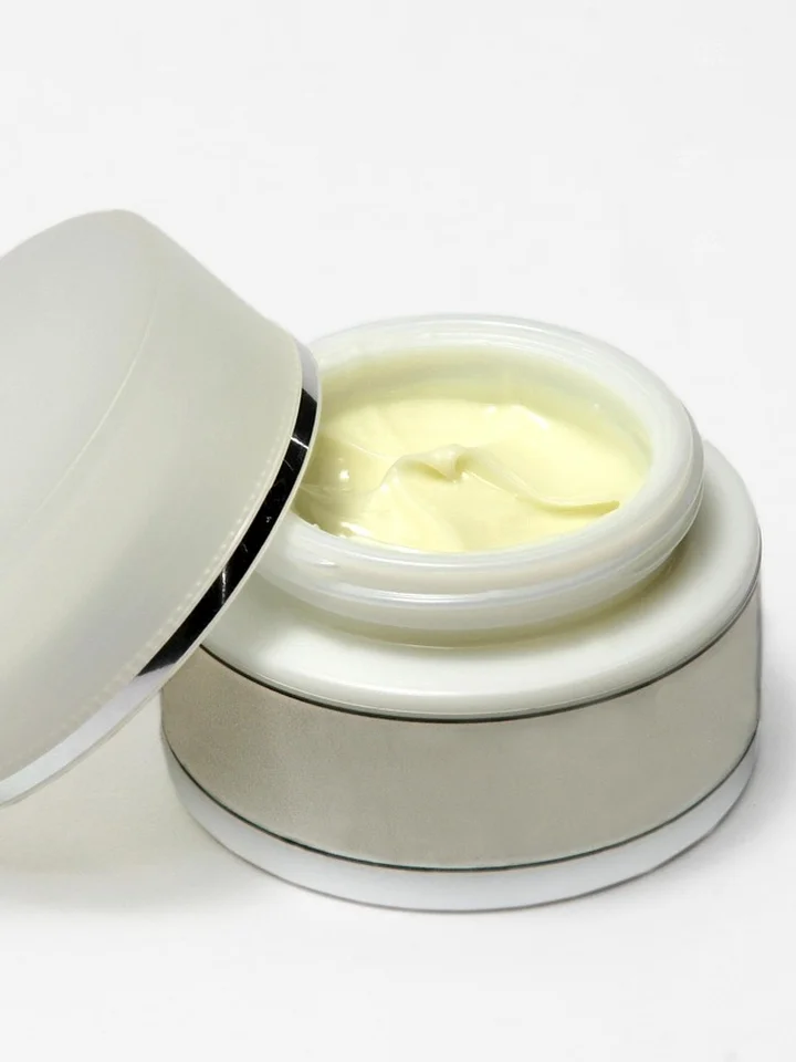 Open jar of pale yellow azelaic acid cream in a white container against a white background