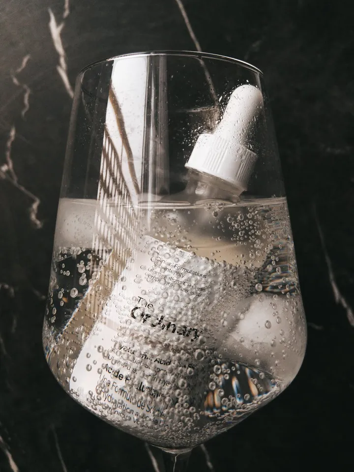 Dropper bottle in a clear glass with bubbles on a dark marble surface.