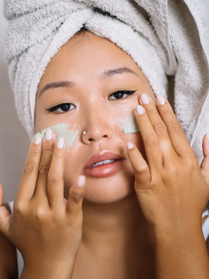 Close-up of a person with a towel wrapped around their head applying under-eye gel patches