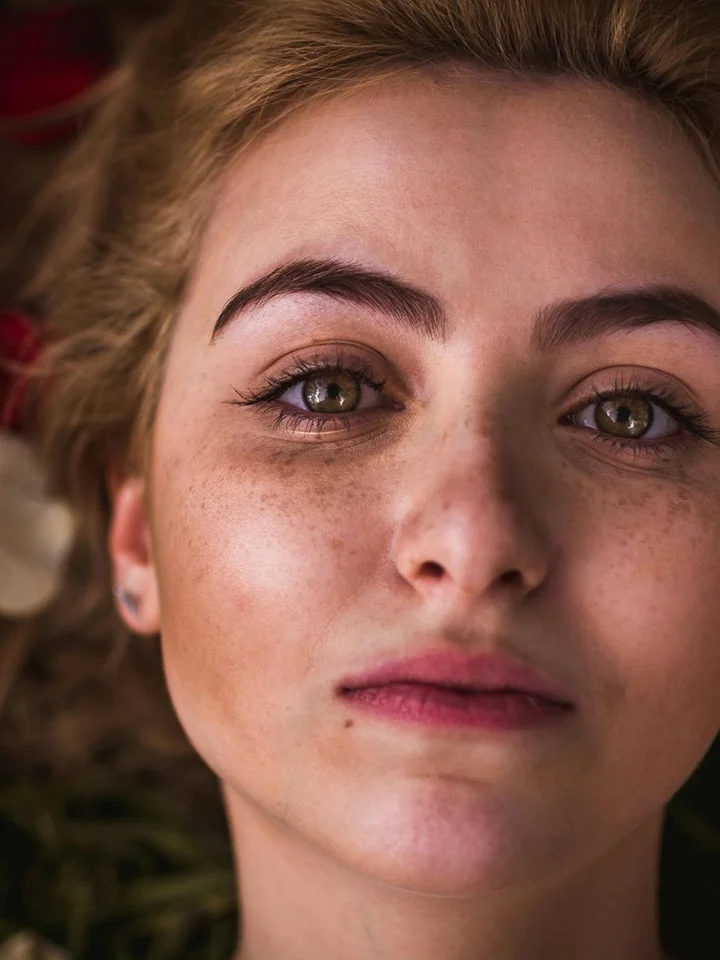 Close-up portrait of a young woman with freckles and light brown hair, neutral expression.
