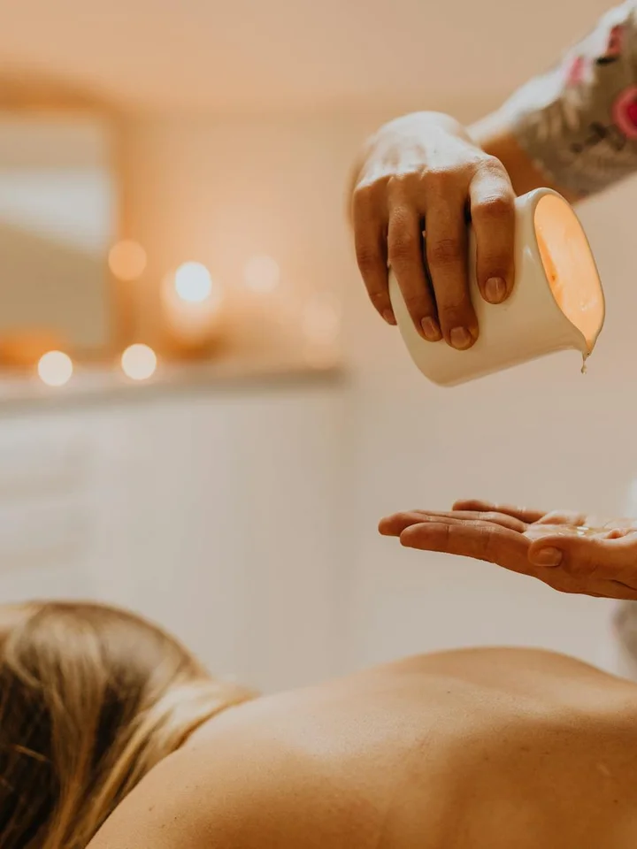 Close-up of a person pouring lotion or oil into their palm during a skincare treatment, with a soft, candle-lit background.