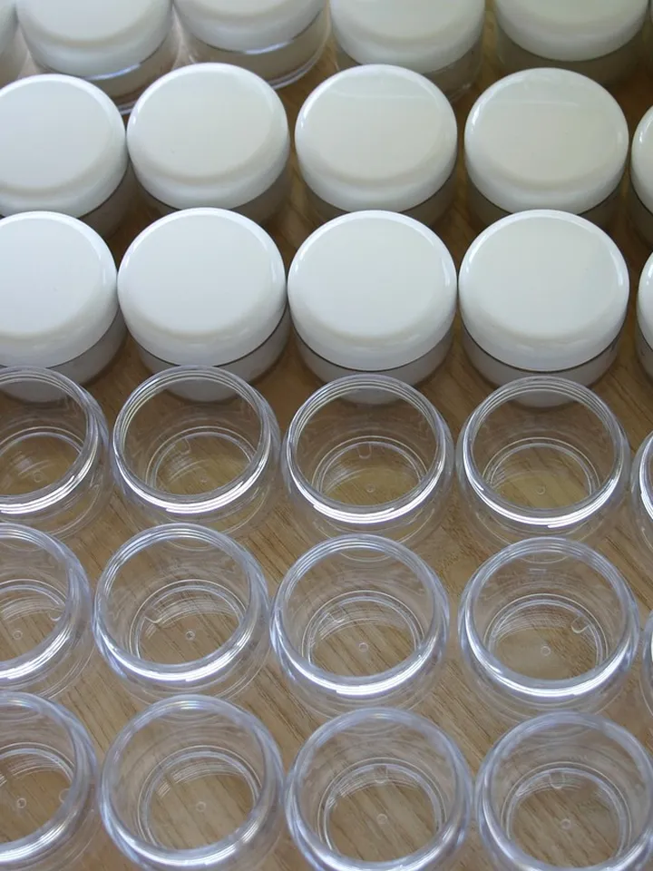 Row of small clear cosmetic jars with white lids arranged on a wooden surface.