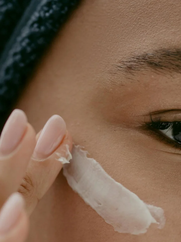 Close-up of a person applying a white cream to their cheek with two fingers.