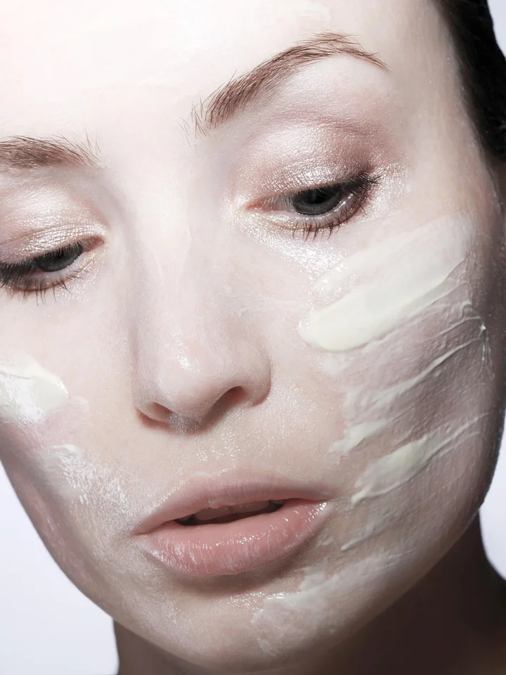 Close-up of a woman's face with a thick cream applied to the cheeks as part of a nighttime skincare routine.