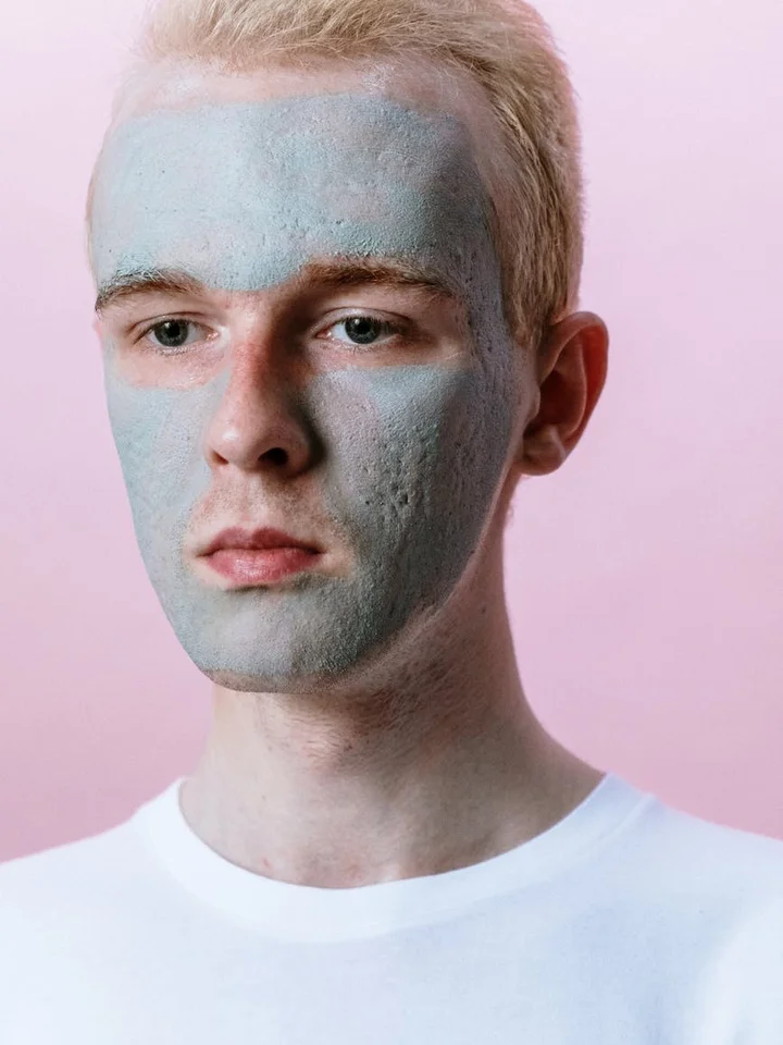 Close-up of a person wearing a light blue facial mask over the face, set against a pink backdrop.