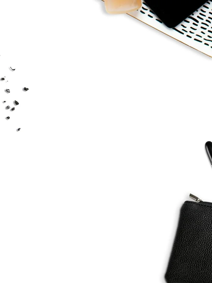 Flat lay of makeup items on a white background: a black textured pouch on the right, a partial keyboard in the top corner, and scattered powder specks on the left.