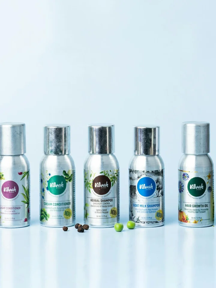 Line of small silver-capped hair care bottles with green labels lined up on a white reflective surface