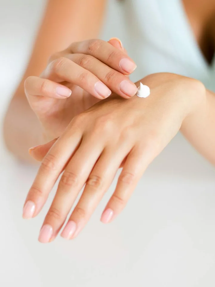 Close-up of hands with a small dab of white cream on the back of one hand being spread by the other hand