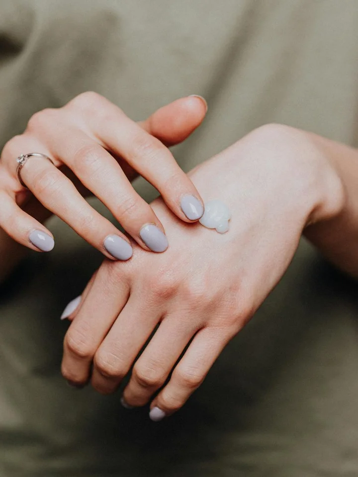 Close-up of hands with a small amount of moisturizer on the back of one hand, ready to apply.