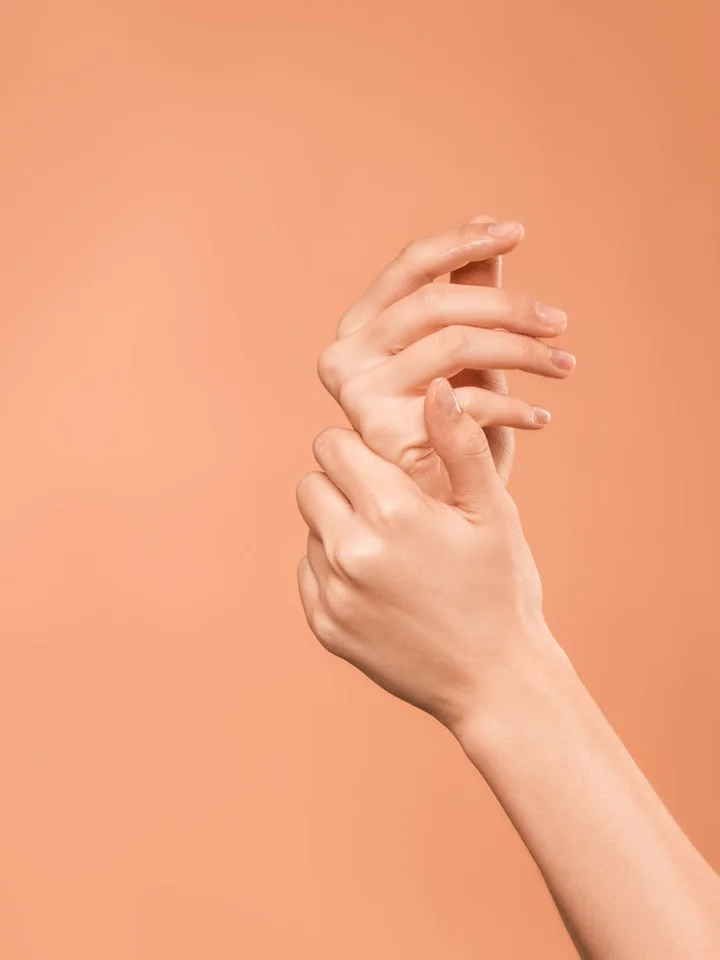 Close-up of interlaced hands against a peach background, suggesting skin elasticity and suppleness.