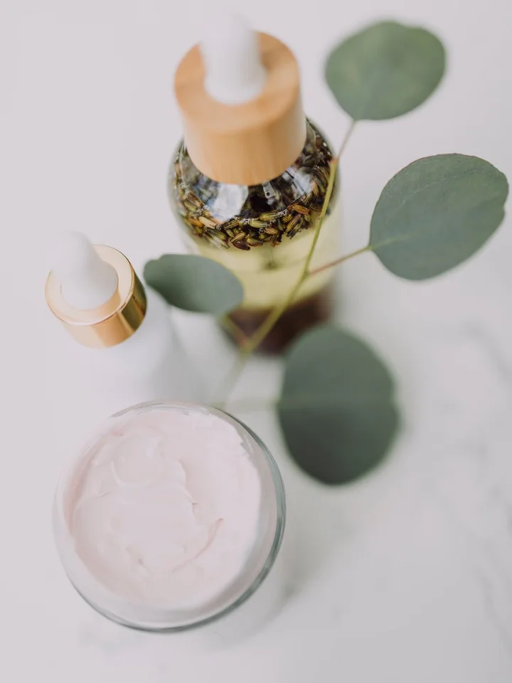 A minimal skincare setup featuring a jar of cream, two dropper bottles, and eucalyptus leaves.