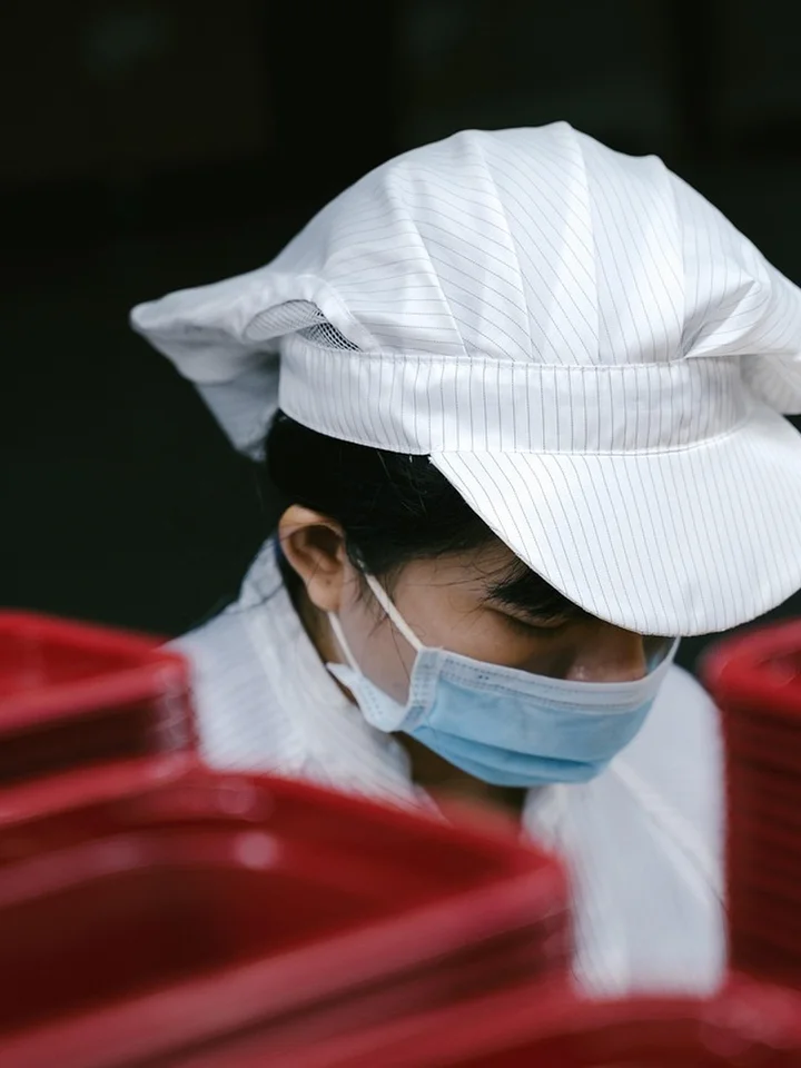 A laboratory worker wearing a white cap, protective mask, and gown examines red sample containers, highlighting the clinical setting where skincare ingredients are studied for anti-inflammatory effects.