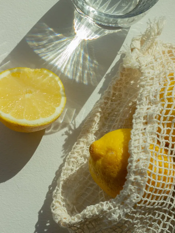 Lemons and a glass of water with sunlight reflections on a light surface, illustrating vitamin C and skincare context.