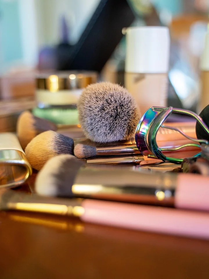 Close-up of makeup brushes and beauty products arranged on a vanity with a blurred colorful background.