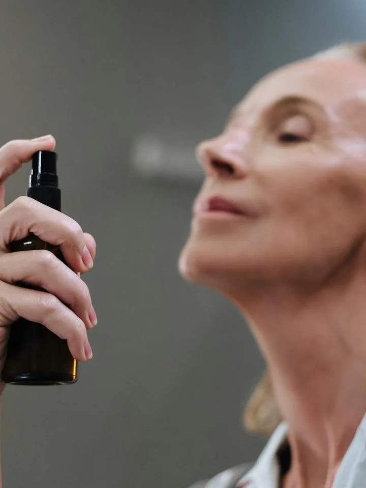 Close-up of a person preparing to apply mandelic acid toner from a dark bottle with a spray nozzle