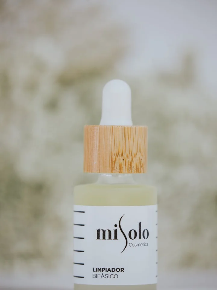 Close-up of a dropper bottle labeled Mi Solo Cosmetics with pale yellow liquid and a wooden cap; the label reads 'limpiador bifásico'.