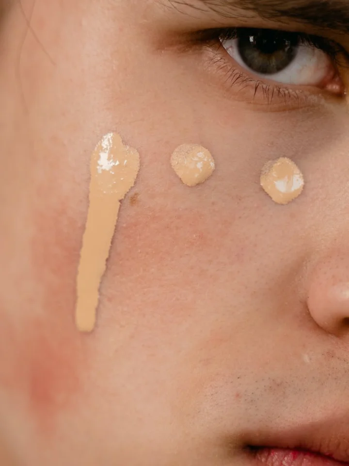Close-up of a person's cheek with three beige swatches of foundation or concealer placed near the eye