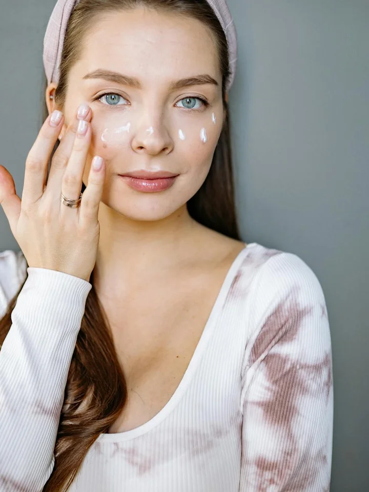 Close-up portrait of a young woman applying skincare cream to her face with dotted white cream on her cheeks