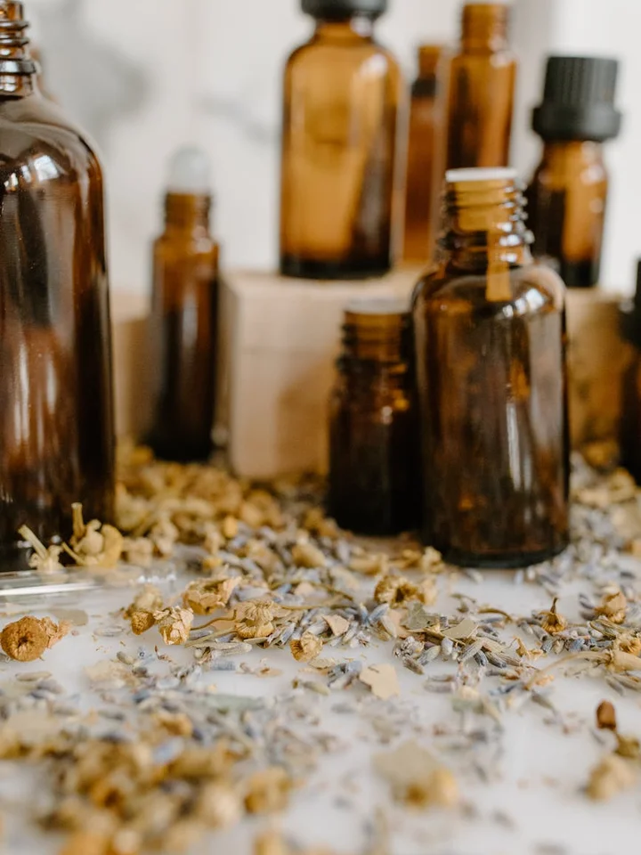 Amber glass bottles of essential oils on a surface with scattered dried botanicals