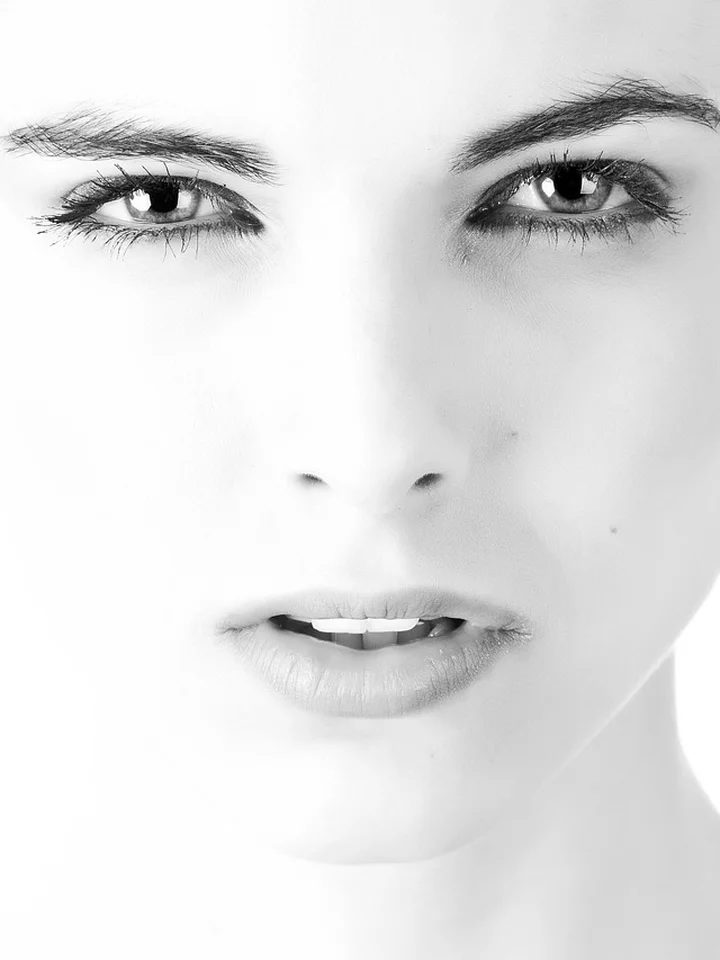 Close-up black-and-white portrait of a woman's face with even lighting, focusing on clear, smooth skin.