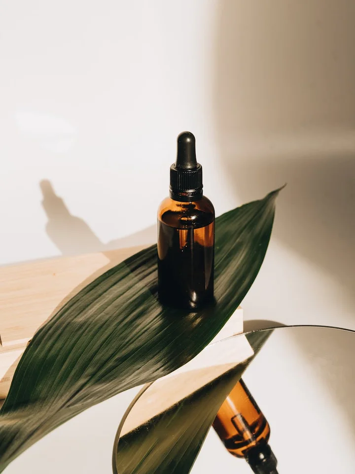 Brown glass dropper bottle of niacinamide serum resting on a large green leaf, bathed in soft natural light.