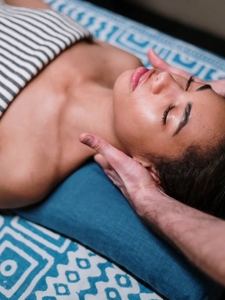 Relaxed person lying on a blue patterned surface with a hand supporting their head and eyes closed.