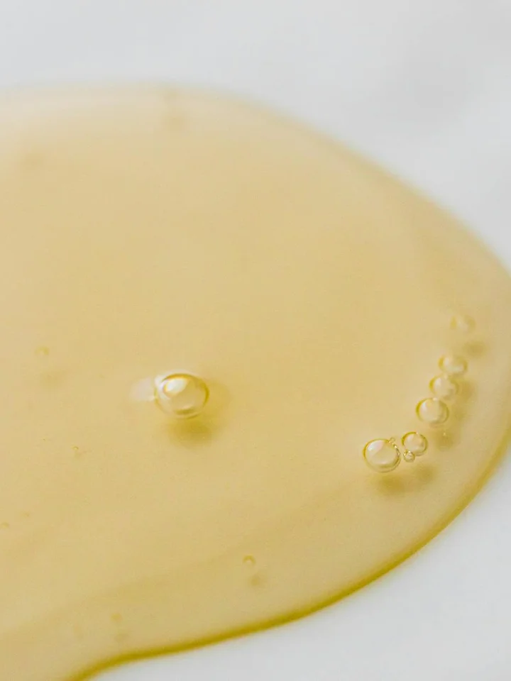 Close-up of a pale yellow oil droplet spread on a white surface