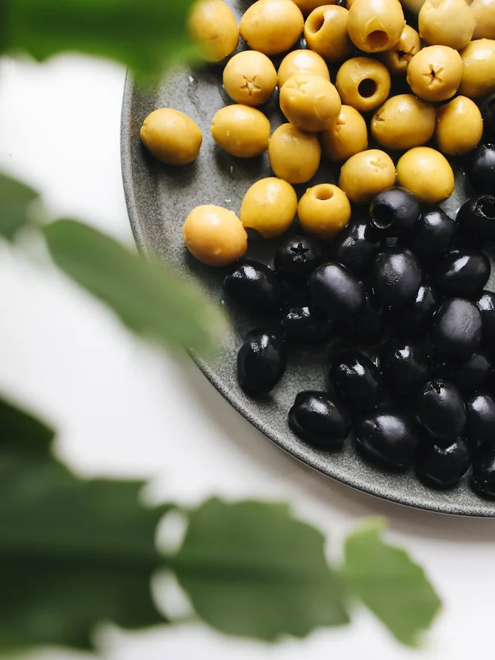 Plate of yellow and black olives with green leaves in the foreground.