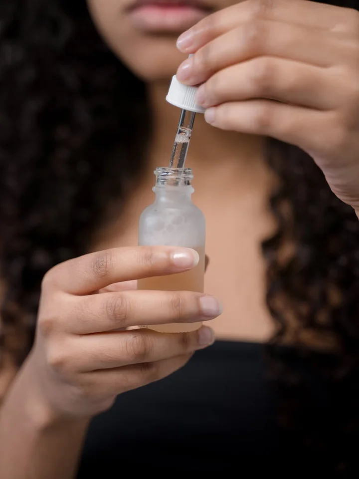 A person holding a small bottle and using a dropper to apply serum to their skin