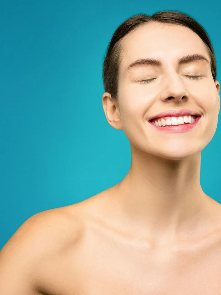 Smiling person with eyes closed against a teal background, conveying calm and wellness.