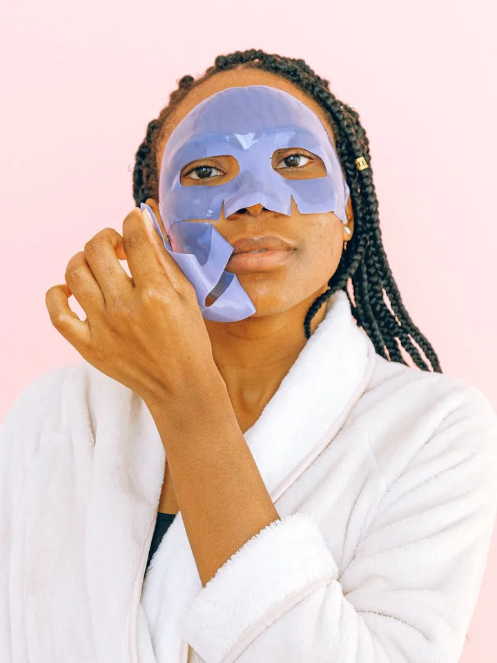 Person in a white robe wearing a blue sheet mask, illustrating a pore-safe skincare routine.