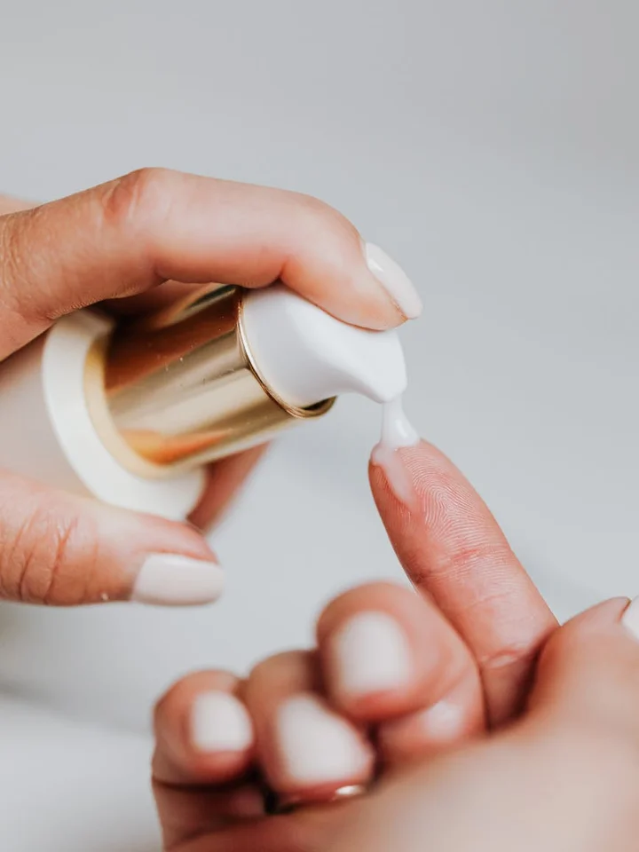Close-up of hands squeezing white cream from a bottle onto a finger for skincare application.