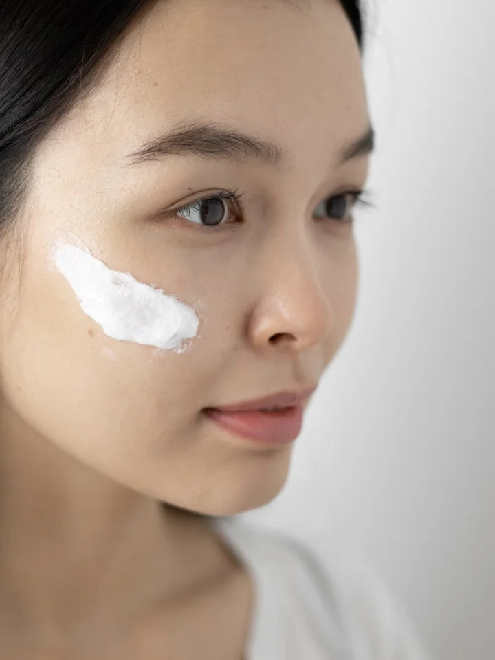 Close-up of a woman's face with a white cream patch applied to the cheek, representing topical retinoid use.