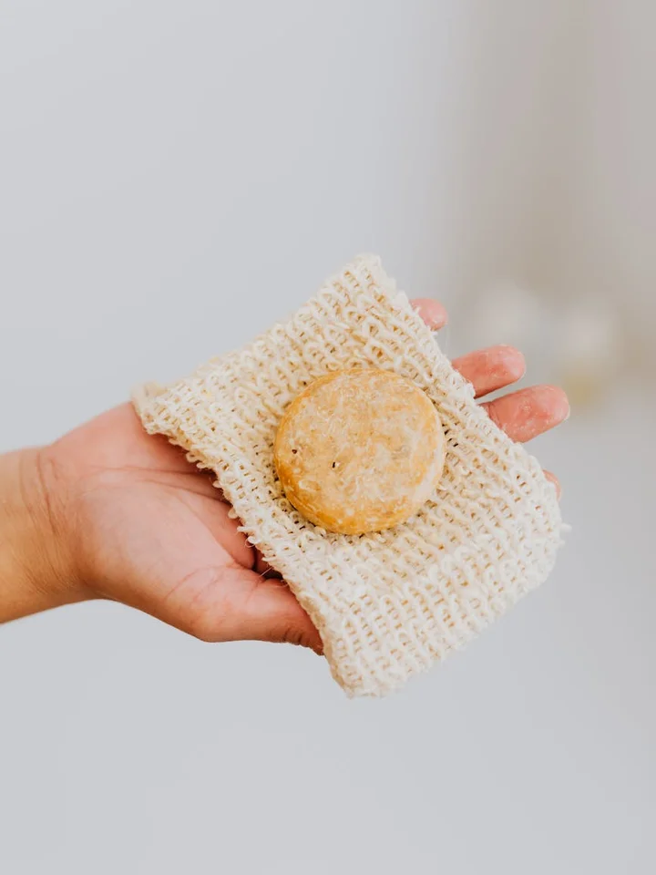 A bar of soap resting on a woven washcloth held in a person's hand, against a soft neutral background.