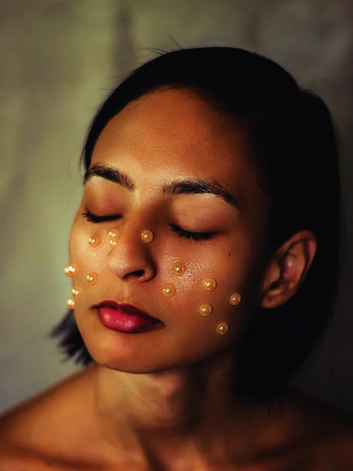 Close-up portrait of a woman with small droplets of skincare product on her cheeks during a routine.