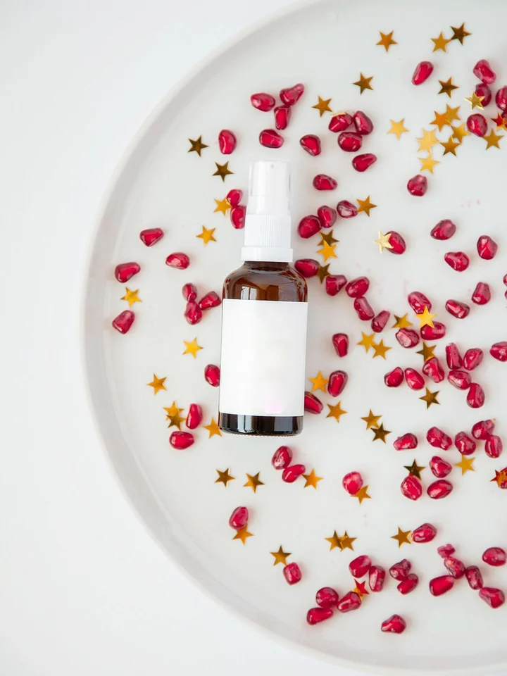 Brown glass dropper bottle on a white plate surrounded by pink petals and gold star confetti.