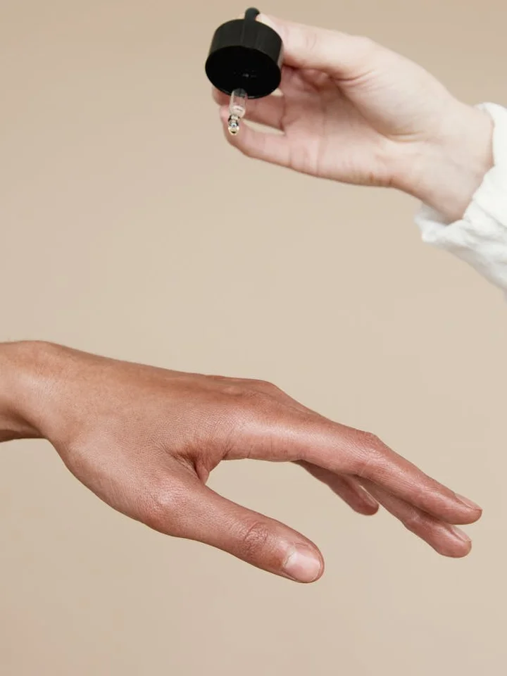 Close-up of a hand with a dropper releasing serum against a beige background.