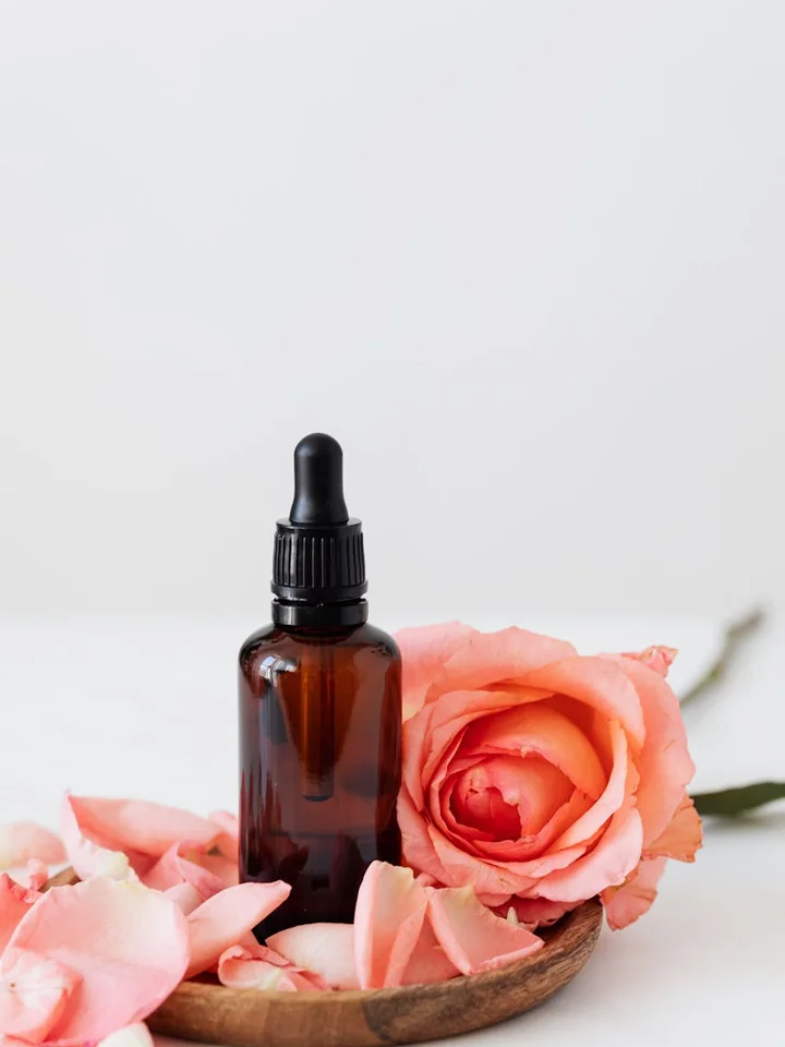 Brown glass dropper bottle surrounded by pink rose petals on a light background, symbolizing skincare ingredients