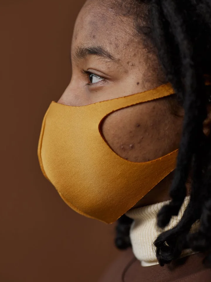 Profile of a person wearing a mustard-yellow face mask, looking to the left.