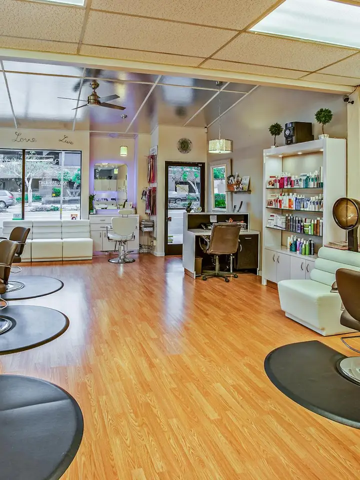 Interior of a modern hair salon with wooden floors, styling chairs, mirrors, and shelves stocked with hair care products.