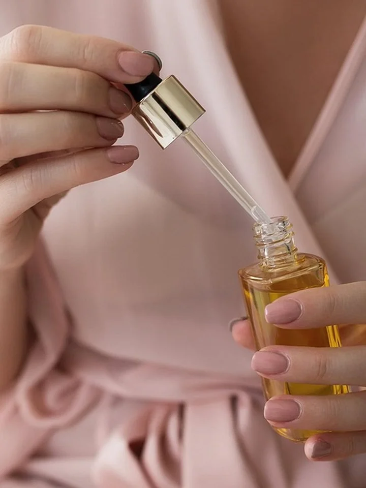 Close-up of hands holding a dropper above a small amber glass bottle filled with yellow serum.