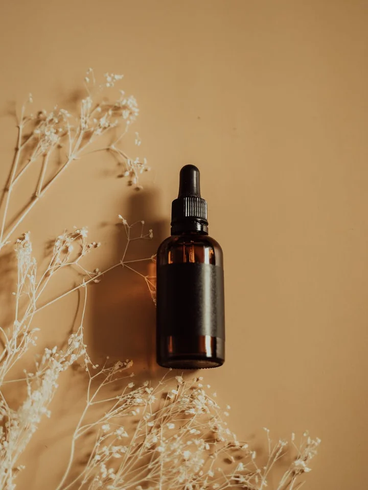 Brown glass dropper bottle of hyaluronic acid serum on a beige background, surrounded by dried white flowers
